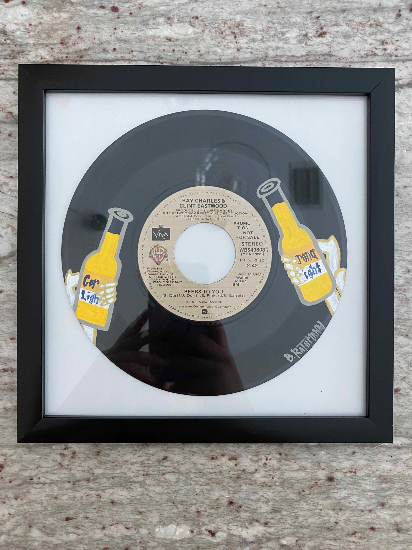 The Beers to You Record is an acrylic painting of two skeletons giving a cheers with Corona Light beer. This is a vinyl record painting that will add a fun and bold aesthetic with your decor. This work was done on a repurposed vinyl record bought at a local thrift store. This was inspired by the music listed on the vinyl album. The frame is included with purchase. Measurements: 8"x8"