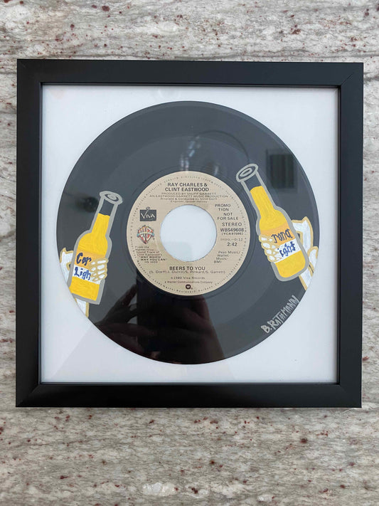The Beers to You Record is an acrylic painting of two skeletons giving a cheers with Corona Light beer. This is a vinyl record painting that will add a fun and bold aesthetic with your decor. This work was done on a repurposed vinyl record bought at a local thrift store. This was inspired by the music listed on the vinyl album. The frame is included with purchase. Measurements: 8"x8"